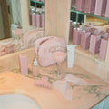 Bow Barrette in Sheer Baby Mauve on bathroom counter with halo hair oil, dream creme, big effing clip in pink sugar, cocktail glass with pink liquid, and pouch