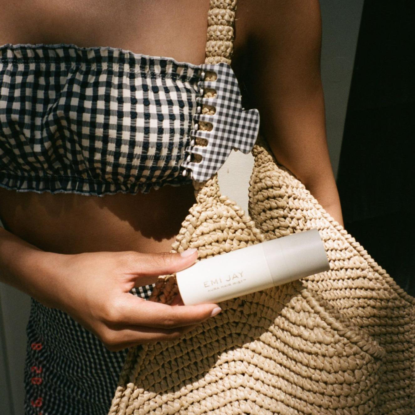 model holding aura hair mist with Big Effing Clip in Navy Gingham clipped to strap of purse