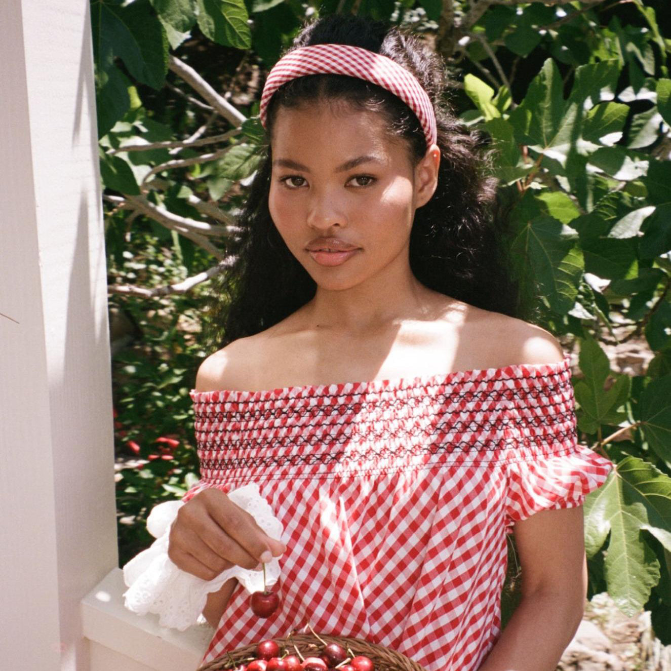 model holding cherry while standing with Halo Headband in Cherry Gingham in hair