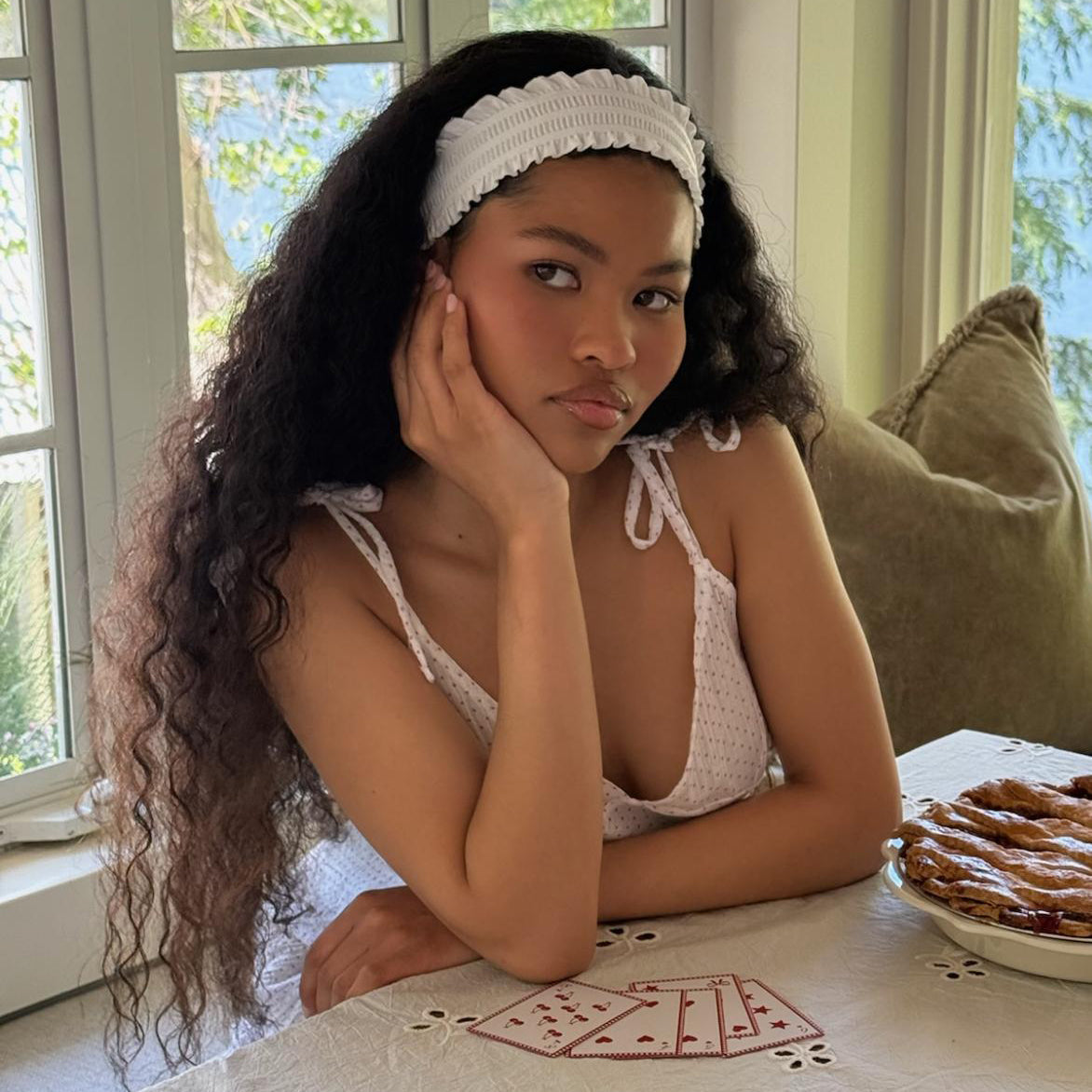 model with hand on cheek and Ruffle Headband in Daffodil in hair sitting at table in front of playing cards and apple pie